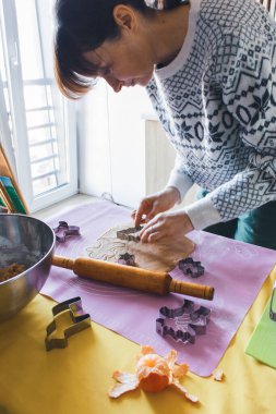 Noel kazaklı bir kadın ev mutfağında farklı şekillerde zencefilli kurabiye yapıyor. Masada kadın aşçıyla merdane ve kurabiye formu. Ev yapımı kurabiyeler hazırlanıyor. Noel kurabiyesi yapan kadın. Noel hazırlığı.