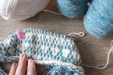 Norveçli kadın ellerine örgü örüyor. Ellerinde örgü iğneleri ve güzel örgü desenleri olan bir kız. Beyaz ve gök mavisi desenli bir kadın. Örgü hobisi. Örgü giyme konsepti. Leke süveter deseni