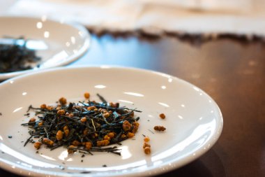 Beyaz tabakta kurumuş yeşil çay yaprakları. Japon kuru çay tatma töreni. Bir yığın Sencha çayı. Sağlıklı yaşam tarzı kavramı. Asya çay kültürü.