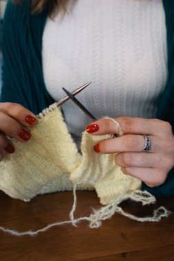 Ellerinde örgü iğneleri ve sarı pamuklu örgü ören kadınlar. Örgü ören kadın, iplik ve sarı örgü elbiseli. Dikiş işlemi devam ediyor. Örgü hobisi. Örgü işi.. 
