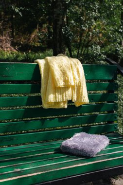 Sarı pamuklu hırka ve yeşil bankta gri kitap kapağı. Yumuşak sarı örgü süveter ve parktaki bankta kabarık bir kitap. Büyük şehir modası. Yaz örgü modası. Samimi bir hobi. Ürün konsepti. 