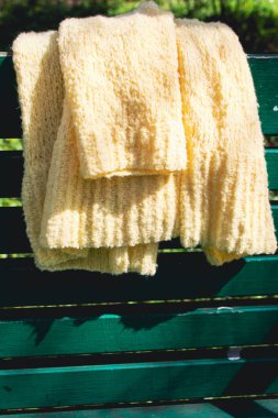 Yeşil bankta sarı pamuk örülmüş hırka. Parktaki bankta yumuşak sarı örülü süveter. Büyük şehir modası. Yaz örgü modası. Samimi bir hobi. Ürün konsepti. 