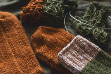 İplik yumağı ve örgü iğneleriyle örülmüş sıcak çoraplar. Koyu yeşil çarşafta çizgili yün çoraplar. Samimi sonbahar renkleri. Örgü örerek kapatın. Örgü hobisi. Örgü giyme konsepti. İğne işi arkaplanı. 