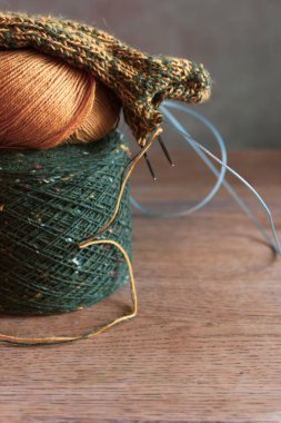 İplik yumağı ve örgü iğneleriyle örülmüş sıcak çoraplar. Yün çorap örme işlemi. Samimi sonbahar titreşimleri. Ahşap masada sarı ve yeşil tüvit iplik. Örgü hobisi. Örgü giyme konsepti. İğne işi arkaplanı.