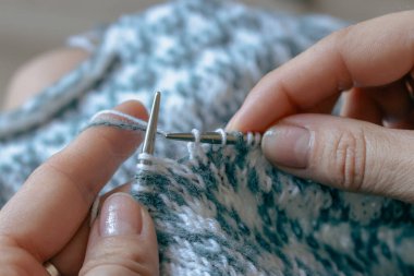 Norveçli kadın ellerine örgü örüyor. Ellerinde örgü iğneleri ve güzel örgü desenleri olan bir kız. Beyaz ve gök mavisi desenli bir kadın. Örgü hobisi. Örgü giyme konsepti. Benekli kazak