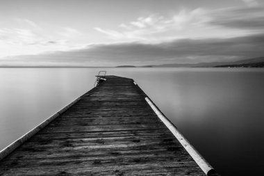 Long exposure view of a pier on a lake with perfectly still water.