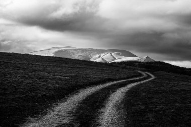 Bulutlu gökyüzünün altında kıvrımlı bir dağ yolu.