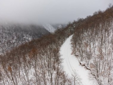 Ormanın ortasında karla kaplı bir dağ yolunun havadan görünüşü.