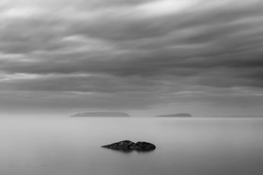 Long exposure view of a rock in Trasimeno lake Umbria, with islands in the background and moody sky. clipart