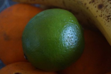 Bir kireç, renginin yoğunluğunu arttıran doğal ışıkla yıkanmış pürüzsüz bir yüzeyde zarifçe durur. Dokulu, hafif engebeli cildi yüzeyinde boncuk boncuk gibi parlayan küçük su damlacıklarıyla çelişiyor.. 