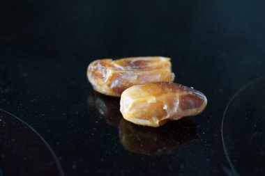 Sıcak renkli bir avuç dolusu hurma doğal bir yüzeye nazikçe uzanır. Derin parıltılarını ve buruşuk dokularını ortaya çıkarır. Parlak ciltleri, doğal şeker bakımından zengin, karşı konulmaz bir tatlılığı çağrıştırıyor.. 