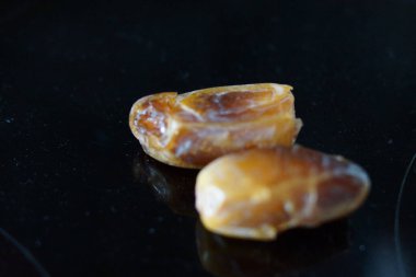 Sıcak renkli bir avuç dolusu hurma doğal bir yüzeye nazikçe uzanır. Derin parıltılarını ve buruşuk dokularını ortaya çıkarır. Parlak ciltleri, doğal şeker bakımından zengin, karşı konulmaz bir tatlılığı çağrıştırıyor.. 