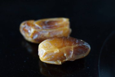 Sıcak renkli bir avuç dolusu hurma doğal bir yüzeye nazikçe uzanır. Derin parıltılarını ve buruşuk dokularını ortaya çıkarır. Parlak ciltleri, doğal şeker bakımından zengin, karşı konulmaz bir tatlılığı çağrıştırıyor.. 