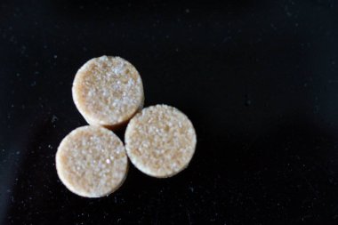 Kahverengi şeker küpleri ışığın altında pırıl pırıl parıldıyor ve mükemmel kübik şekillerini ve narin kristallerini ortaya çıkarıyor. Hafif kumlu dokuları kusursuz parlaklıklarına zıt düşerken ışık yüzeylerinde ince yansımalar yaratıyor.. 