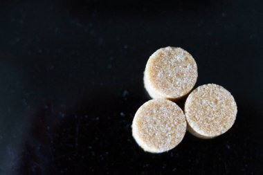 Kahverengi şeker küpleri ışığın altında pırıl pırıl parıldıyor ve mükemmel kübik şekillerini ve narin kristallerini ortaya çıkarıyor. Hafif kumlu dokuları kusursuz parlaklıklarına zıt düşerken ışık yüzeylerinde ince yansımalar yaratıyor.. 