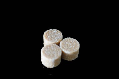 Kahverengi şeker küpleri ışığın altında pırıl pırıl parıldıyor ve mükemmel kübik şekillerini ve narin kristallerini ortaya çıkarıyor. Hafif kumlu dokuları kusursuz parlaklıklarına zıt düşerken ışık yüzeylerinde ince yansımalar yaratıyor.. 