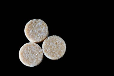 Kahverengi şeker küpleri ışığın altında pırıl pırıl parıldıyor ve mükemmel kübik şekillerini ve narin kristallerini ortaya çıkarıyor. Hafif kumlu dokuları kusursuz parlaklıklarına zıt düşerken ışık yüzeylerinde ince yansımalar yaratıyor.. 