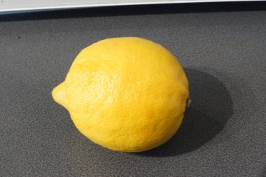 Parlak sarı bir limon zarif bir şekilde parlak bir yüzeye oturur, ışığı yakalar ve hafif desenli cildini ön plana çıkarır. Altın parıltısı tazeliği ve canlılığı çağrıştırırken, keskin aroması görüntüde neredeyse elle tutulur gibi görünüyor..