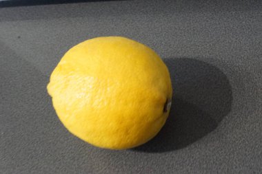 Parlak sarı bir limon zarif bir şekilde parlak bir yüzeye oturur, ışığı yakalar ve hafif desenli cildini ön plana çıkarır. Altın parıltısı tazeliği ve canlılığı çağrıştırırken, keskin aroması görüntüde neredeyse elle tutulur gibi görünüyor..