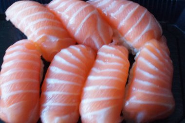 Çok güzel düzenlenmiş somon suşisi, yeni hazırlanmış ve ince bir tabağa güzelce yerleştirilmiş. Somon dilimleri ışığın altında parıldıyor, yumuşak dokularını ve canlı renklerini sergiliyorlar..