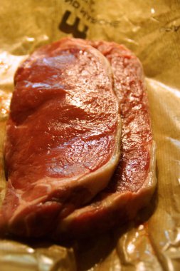 A generous cut of ribeye steak, beautifully marbled, rests on a rustic wooden board. The tender fibers and deep color of the meat highlight the richness of this premium cut, poised to deliver full flavor.
