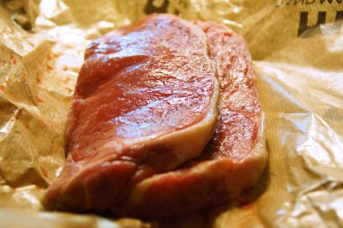 A generous cut of ribeye steak, beautifully marbled, rests on a rustic wooden board. The tender fibers and deep color of the meat highlight the richness of this premium cut, poised to deliver full flavor.