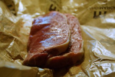 A generous cut of ribeye steak, beautifully marbled, rests on a rustic wooden board. The tender fibers and deep color of the meat highlight the richness of this premium cut, poised to deliver full flavor.