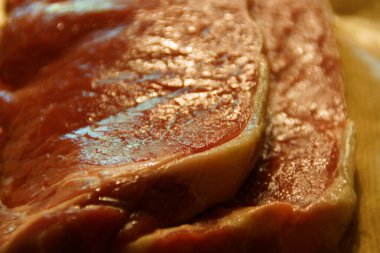 A generous cut of ribeye steak, beautifully marbled, rests on a rustic wooden board. The tender fibers and deep color of the meat highlight the richness of this premium cut, poised to deliver full flavor.