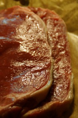 A generous cut of ribeye steak, beautifully marbled, rests on a rustic wooden board. The tender fibers and deep color of the meat highlight the richness of this premium cut, poised to deliver full flavor.