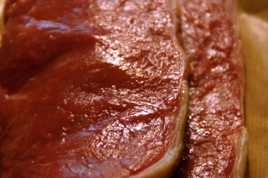 A generous cut of ribeye steak, beautifully marbled, rests on a rustic wooden board. The tender fibers and deep color of the meat highlight the richness of this premium cut, poised to deliver full flavor.