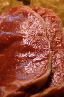 A generous cut of ribeye steak, beautifully marbled, rests on a rustic wooden board. The tender fibers and deep color of the meat highlight the richness of this premium cut, poised to deliver full flavor.