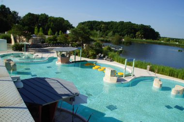 Işıl ışıl bir gökyüzünün altında, geniş bir halka açık yüzme havuzu uzanıyor, rahat yüzücüler ve renkli şezlonglarla dolu. Fransa.