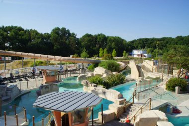 Işıl ışıl bir gökyüzünün altında, geniş bir halka açık yüzme havuzu uzanıyor, rahat yüzücüler ve renkli şezlonglarla dolu. Fransa.