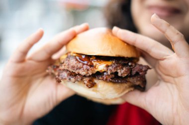 Erimiş peynir ve kaftanla hamburger tutan bir elin yakın çekimi.