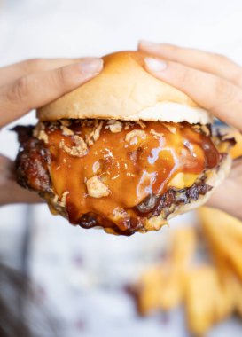 Erimiş peynir ve kaftanla hamburger tutan bir elin yakın çekimi.