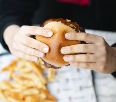 Erimiş peynir ve kaftanla hamburger tutan bir elin yakın çekimi.