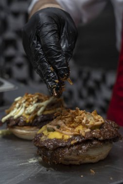 Şef eritilmiş çedarın üstüne turşu ekler Burger köftesi ezer.