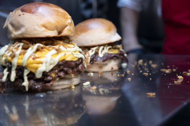 Taze yapılmış, erimiş çedar peynirli, ızgara soğanlı ve parlak bir tezgahta soslu çift ezilmiş burger.