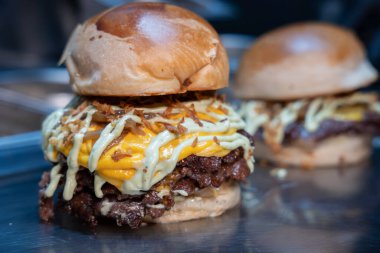 Taze yapılmış, erimiş çedar peynirli, ızgara soğanlı ve parlak bir tezgahta soslu çift ezilmiş burger.