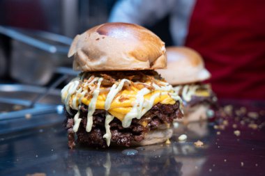 Taze yapılmış, erimiş çedar peynirli, ızgara soğanlı ve parlak bir tezgahta soslu çift ezilmiş burger.