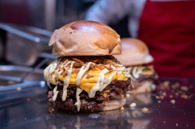 Taze yapılmış, erimiş çedar peynirli, ızgara soğanlı ve parlak bir tezgahta soslu çift ezilmiş burger.