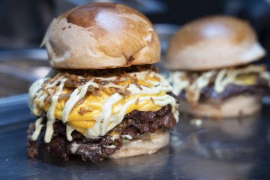 Taze yapılmış, erimiş çedar peynirli, ızgara soğanlı ve parlak bir tezgahta soslu çift ezilmiş burger.