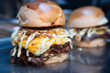 Taze yapılmış, erimiş çedar peynirli, ızgara soğanlı ve parlak bir tezgahta soslu çift ezilmiş burger.