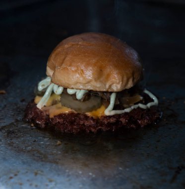 Çedarlı hamburger, turşu, karamelli soğan ve ızgarada sos..