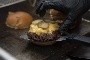 Şef hamburgerciler için erimiş peynirin üzerine turşu ekliyor..