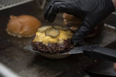 Şef hamburgerciler için erimiş peynirin üzerine turşu ekliyor..