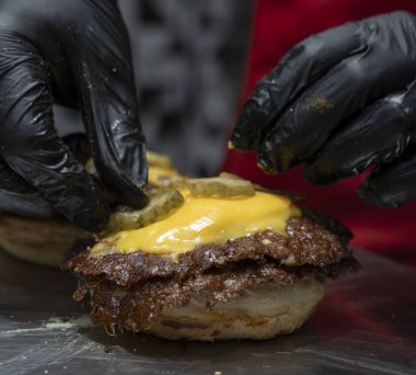 Şef eritilmiş çedarın üstüne turşu ekler Burger köftesi ezer.
