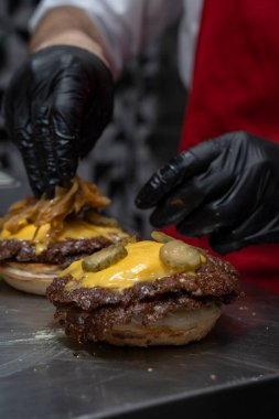 Şef eritilmiş çedarın üstüne turşu ekler Burger köftesi ezer.