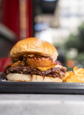 Patates kızartmasıyla servis edilen soğan halkaları ve barbekü soslu gurme Smash Burger.