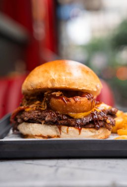 Patates kızartmasıyla servis edilen soğan halkaları ve barbekü soslu gurme Smash Burger.